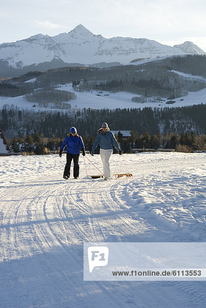 Two women walking with sleds.