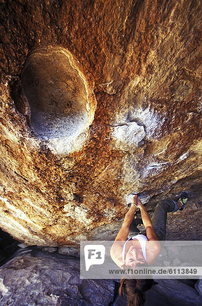 A young woman rockclimbing an overhanging boulder in Hueco Tanks State Historic Park  Texas.