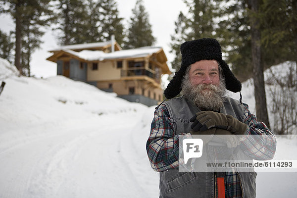Bearded man with snow shovel in front of house in winter  Whitefish  Montana.