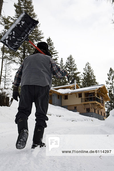 Bearded man with snow shovel in front of house in winter  Whitefish  Montana.