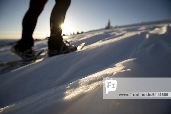 Woman walks in snowshoes at sunset.