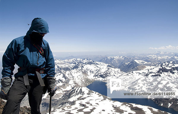 A climber stands at the summit of a peak in the Andes Mountains.