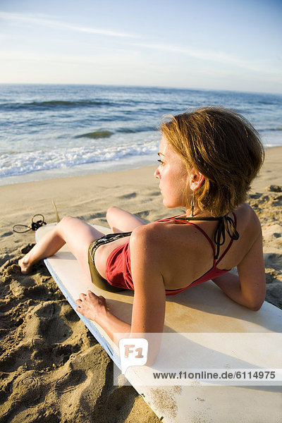 A young woman sits on her surfboard on an isolated beach in Sayulita  Mexico.