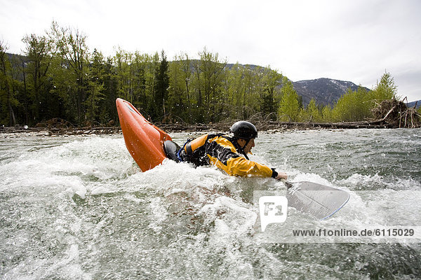 A playboater enjoys a small wave on a river.