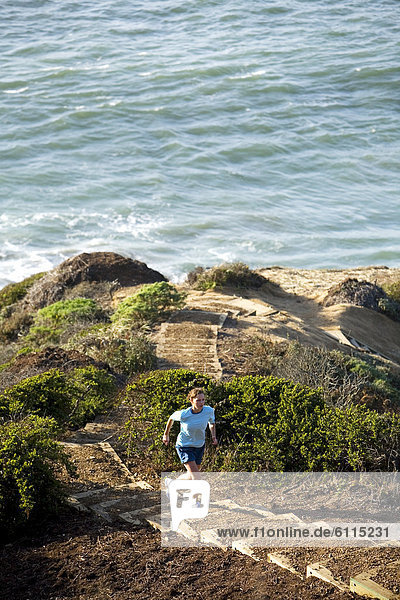A woman running stairs near the ocean.