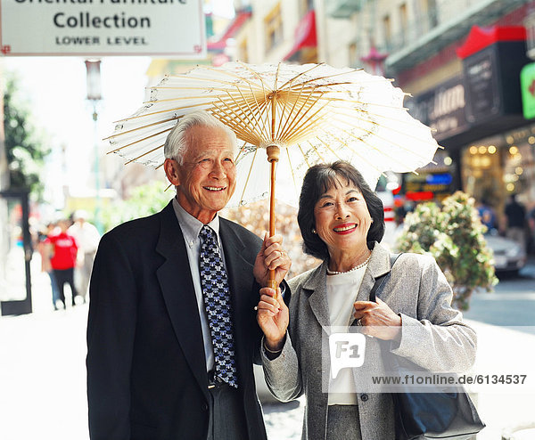 Senior couple with sun umbrella on urban street