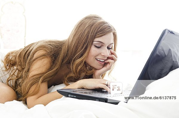Smiling young woman with laptop in bed