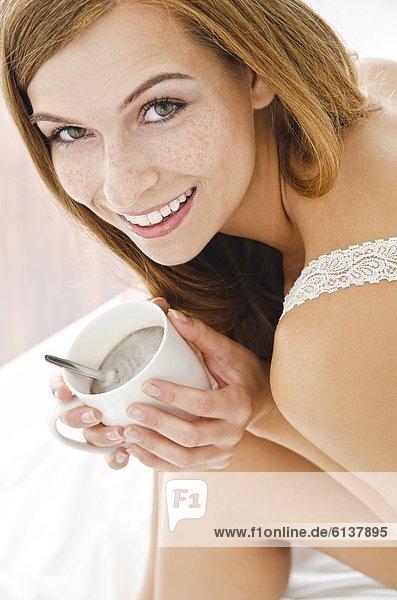 Smiling young woman with cup in bed