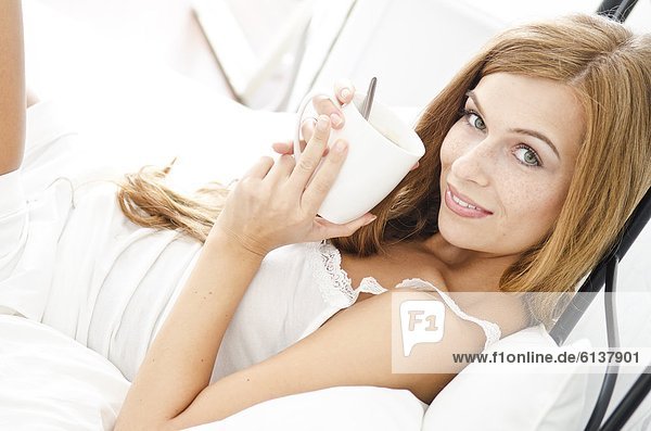 Lächelnde junge Frau mit einer Tasse im Bett