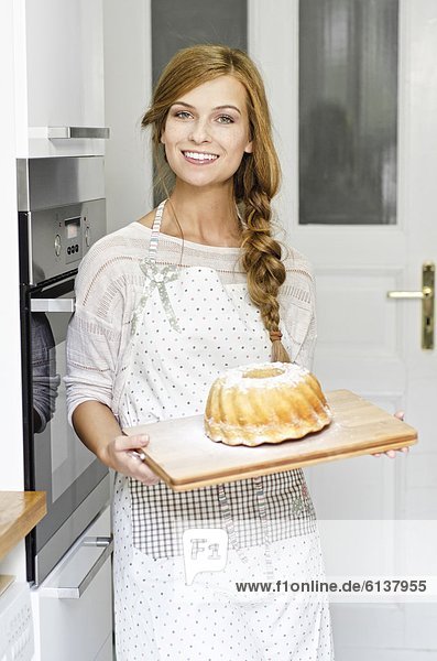 Smiling young woman with cake in kitchen