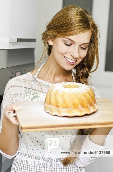 Smiling young woman with cake in kitchen