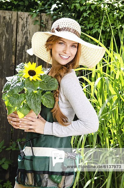 Lächelnde junge Frau mit einer Sonnenblume im Garten