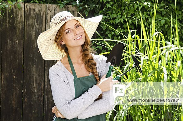 Lächelnde junge Frau mit Sonnenhut und Schürze im Garten