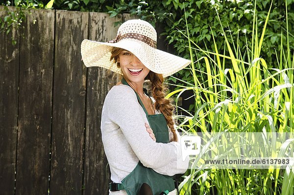 Fröhliche junge Frau mit Sonnenhut und Schürze im Garten