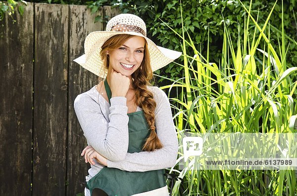 Smiling young woman wearing sunhat and apron in garden