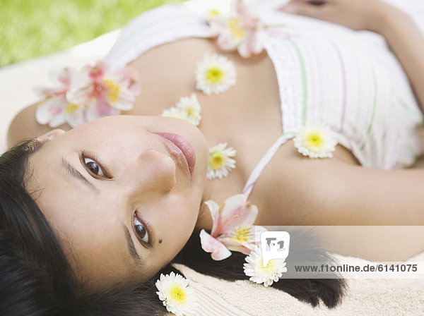 Portrait of woman laying with flowers sprinkled over body