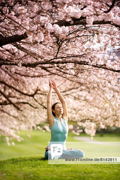 Frau in Lotusstellung unter Kirschbaum  mit erhobenen Armen