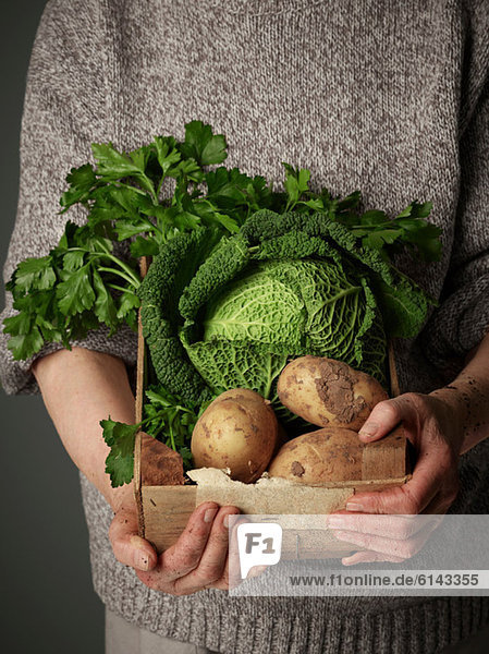 Frau hält Holzkiste mit Gemüse in der Hand