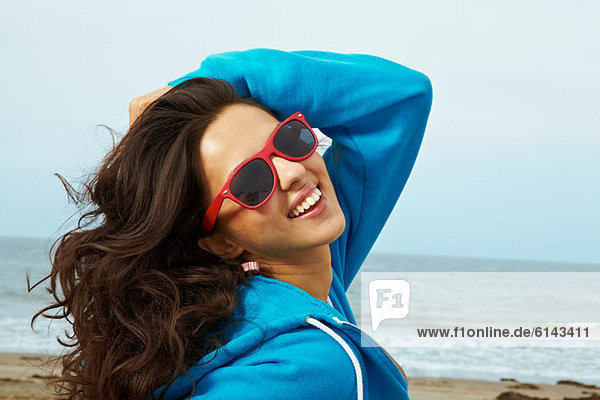 Young woman on beach with hand in hair and red sunglasses