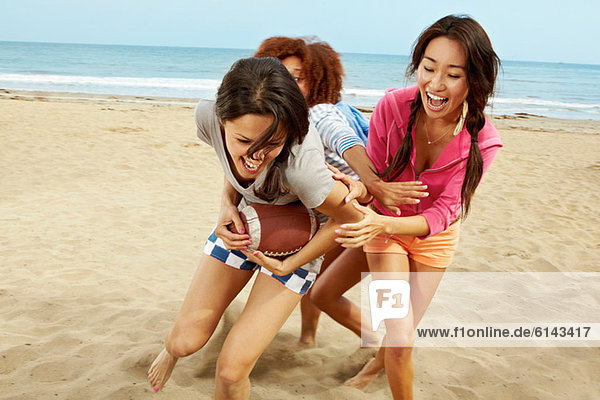 Young female friends playing rugby on beach