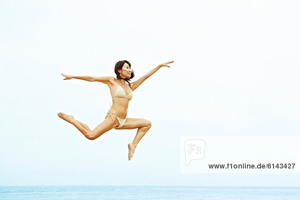 Junge Frau im Bikini beim Springen am Strand