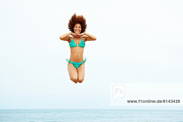 Junge Frau im türkisfarbenen Bikini am Strand springen