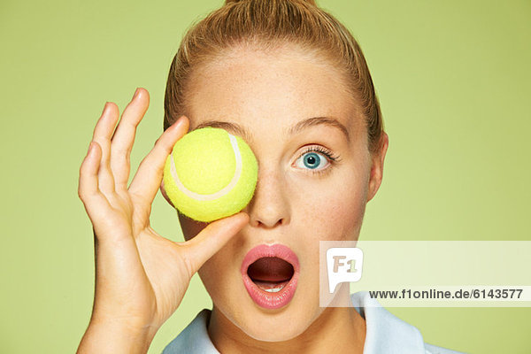 Junge Frau hält Tennisball über das Auge