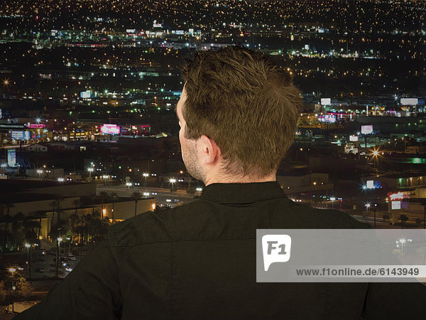 Geschäftsmann blickt von oben auf beleuchtete Stadt bei Nacht  Rückenansicht