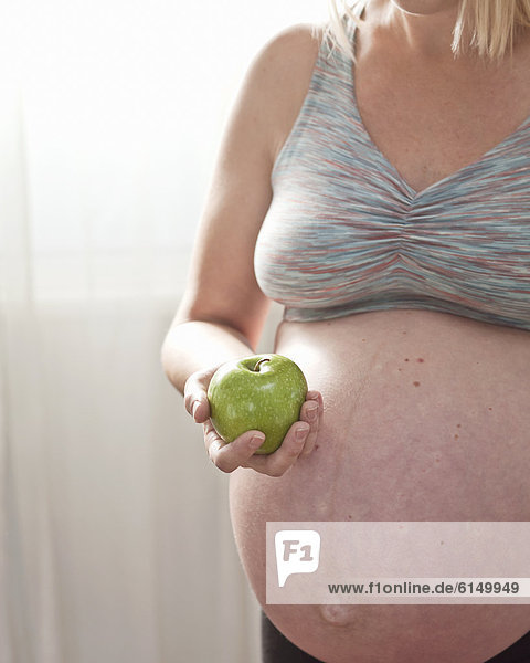 Pregnant Caucasian woman holding green apple