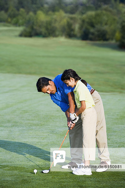 Hispanic father helping daughter play golf