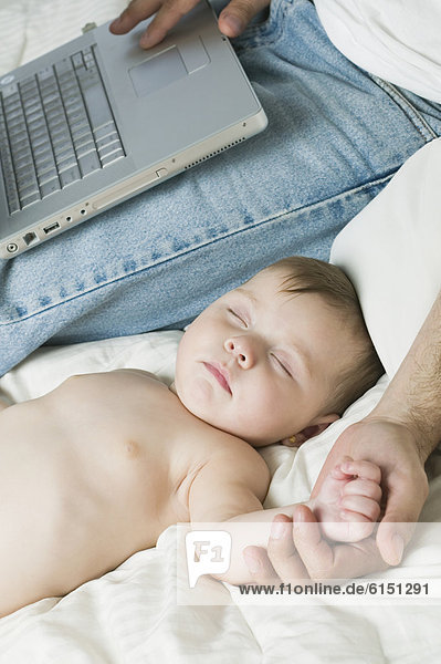 Hispanic father using laptop next to sleeping baby