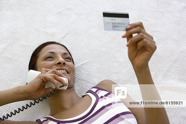 Young woman using credit card over telephone