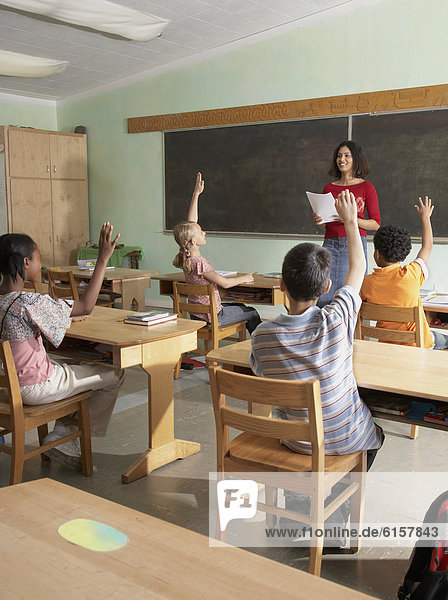 Multi-ethnic students raising hands in class