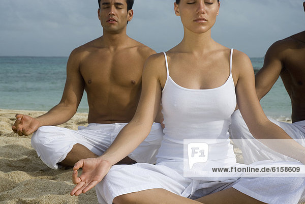 Multi-ethnic friends meditating on beach