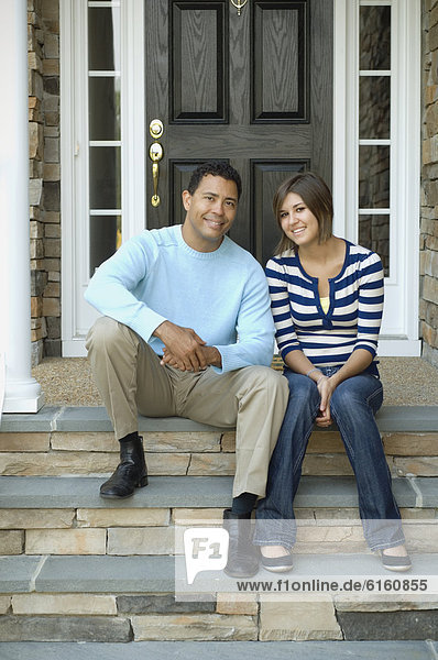Hispanic father and daughter sitting on porch steps