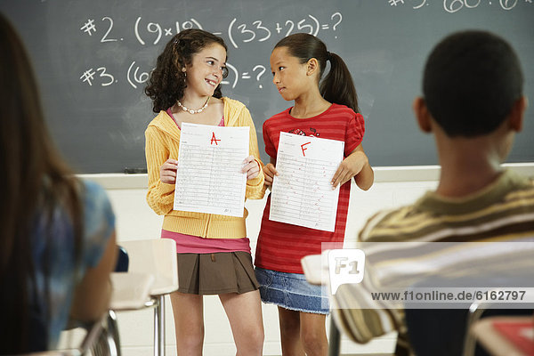 Multi-ethnic girls holding papers in front of class