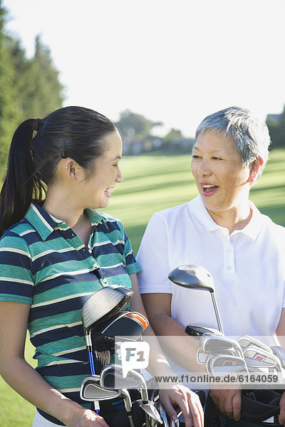 Asian mother and adult daughter holding golf bags