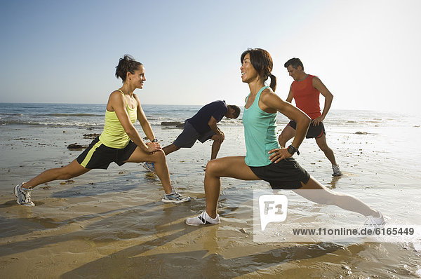 Multi-ethnic runners stretching at beach