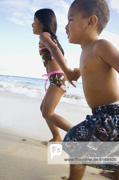 Pacific Islander siblings running on beach