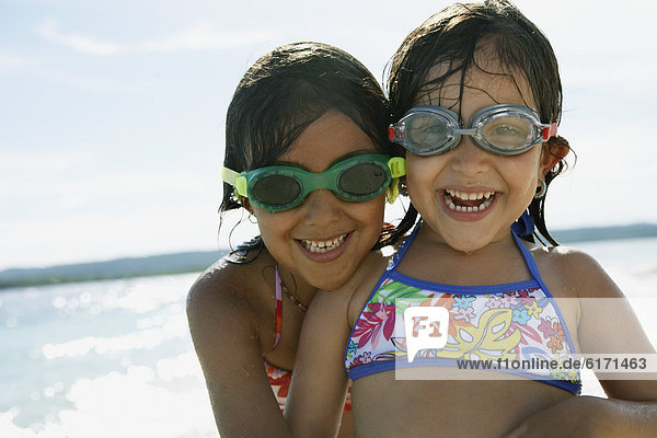 Hispanic sisters wearing goggles at beach