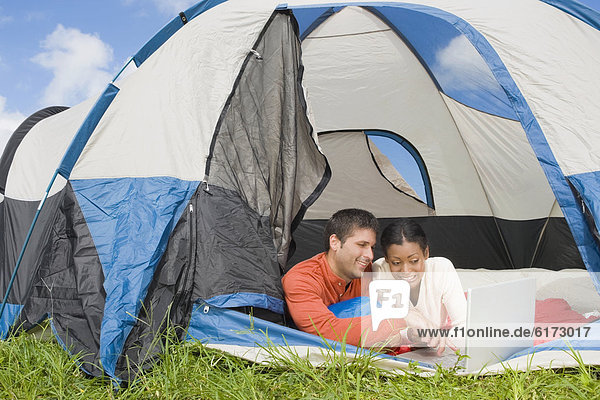 Hispanic couple looking at laptop in tent
