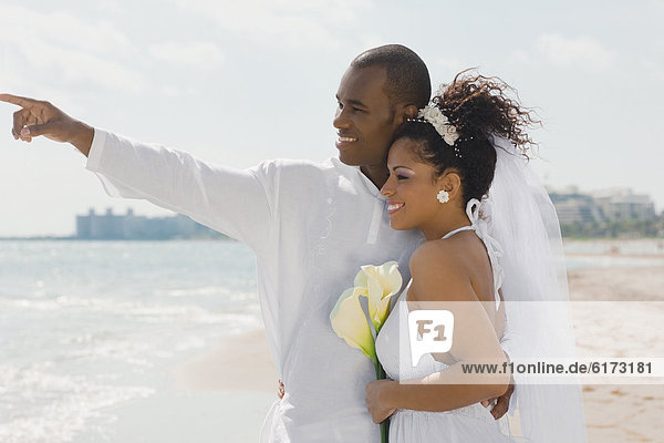 Multi-ethnic bride and groom pointing at beach