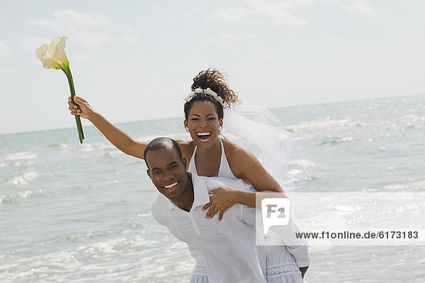 Multi-ethnic bride and groom playing at beach
