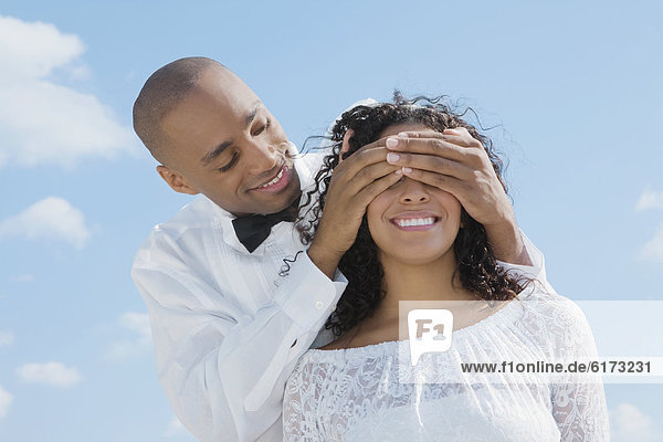 African groom covering bride's eyes