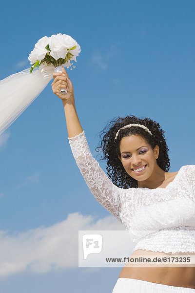 Hispanic bride holding bouquet over head