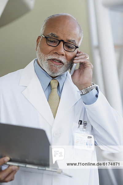 Senior male African doctor talking on cell phone with chart