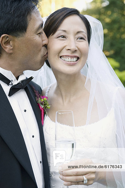 Asian groom kissing bride's cheek