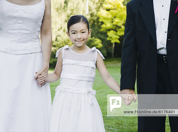 Asian newlyweds holding flower girl's hands