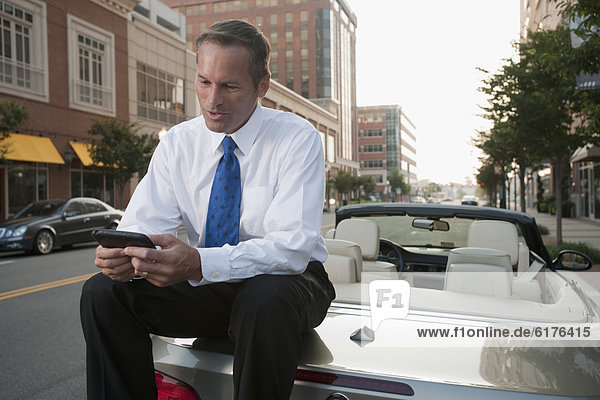Caucasian businessman sitting on car text messaging on cell phone