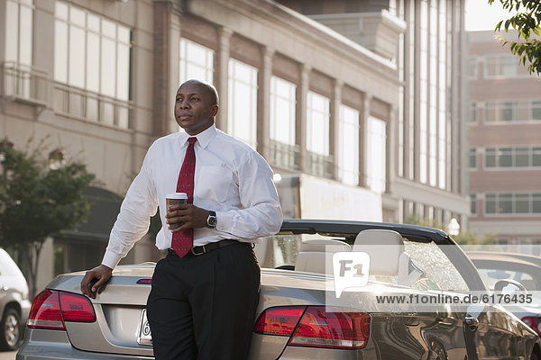 Black businessman drinking coffee near convertible